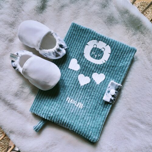chaussons bébé posés sur un carnet de santé bleu avec tête de lion coeurs et prénom dessus