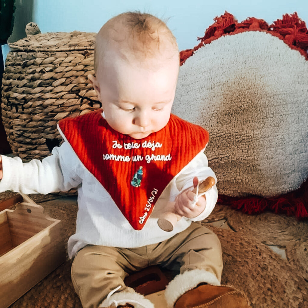 bébé assis portant un bavoir bandana en double gaze ocre avec texte personnalisé